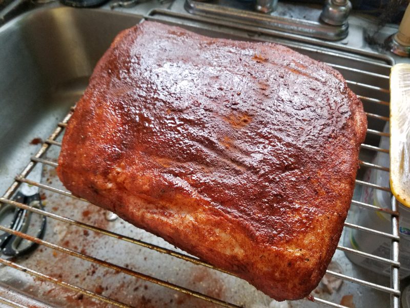 A pork shoulder roast heavily coated in a reddish spice rub, before going into the smoker