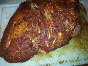 A pork butt roast seasoned with a reddish spice rub on a cutting board, ready for the smoker