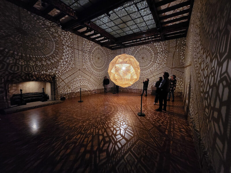 Intricate light patterns projected across a dark room with a glowing orb at the Paine Nature of Light show