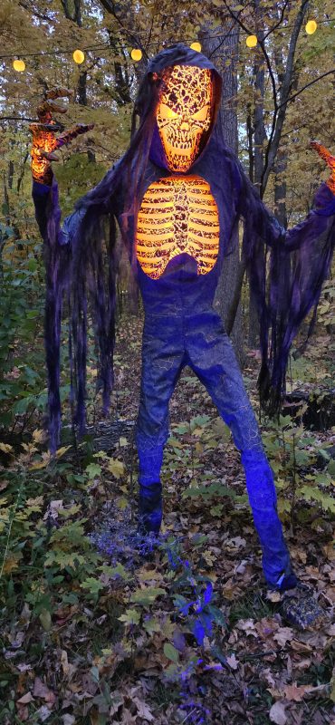Towering skeleton figure with a glowing orange skull and ribcage among the trees