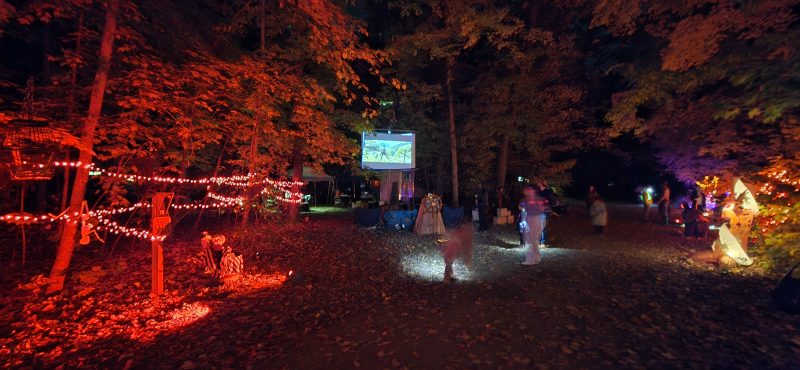 Campground path lit red with an outdoor movie screen and trick-or-treaters