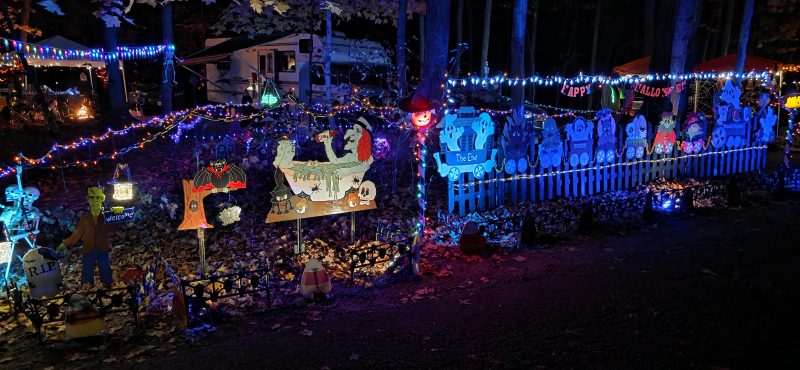Hand-painted plywood Halloween cutouts along a white picket fence with blue lights