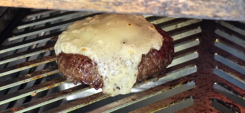 A single hamburger on the broiler rack with cheese melted to a bubbly, golden finish draping over the top