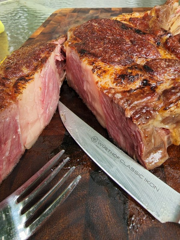 A grilled ribeye steak rested and sliced on a wood cutting board, showing a pink medium-rare center