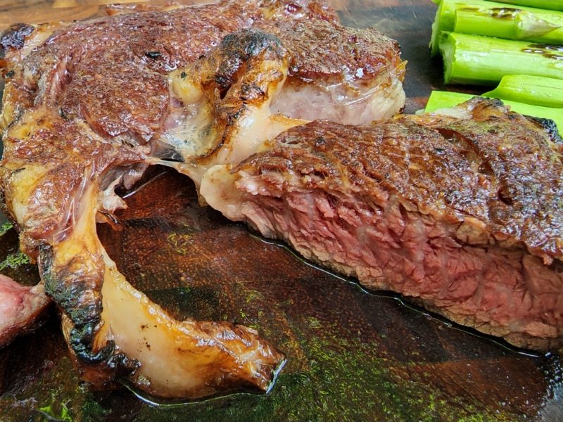 A bone-in ribeye steak sliced on a board with a side of asparagus
