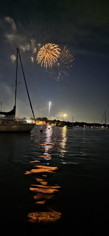 Fireworks over the Neenah harbor with sailboats moored and golden reflections streaking across the water, Riverside Park, Fourth of July 2026