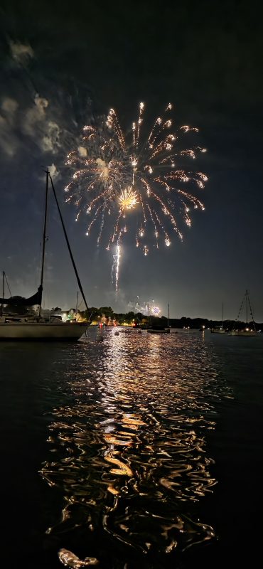 Gold fireworks bursting above moored sailboats on the Neenah channel with long reflections on the water, Fourth of July