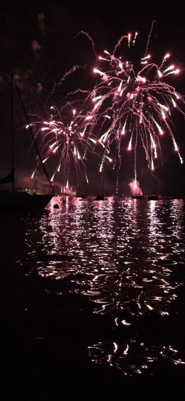 Bright pink and gold fireworks over the Neenah harbor with mirrored reflections on the water, Fourth of July