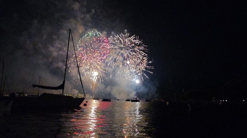 Pink and gold fireworks bursting over Lake Winnebago at Neenah with a sailboat in the foreground, Fourth of July