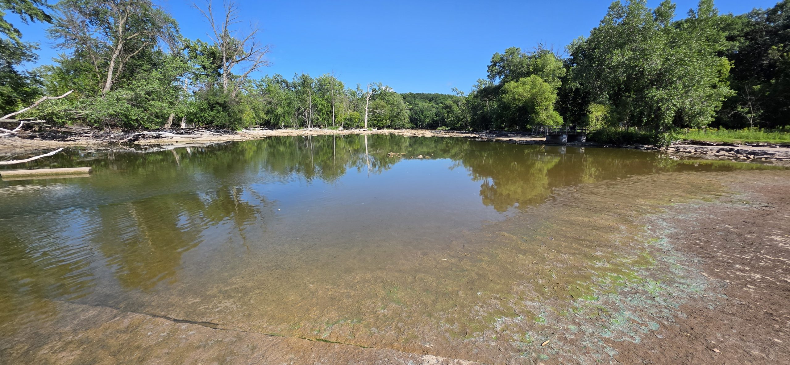 A calm, glassy pool of the Fox River reflecting trees and blue sky at the 1000 Islands Environmental Center in Kaukauna